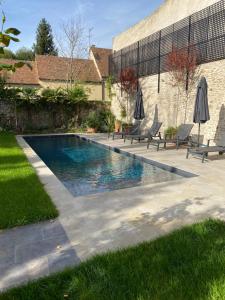 una piscina en un patio con sillas y sombrillas en LA THEBAUDERIE, en Montfort-lʼAmaury