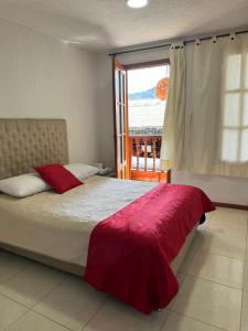 a bedroom with a bed with a red blanket and a window at Hotel La Candelaria in Ráquira