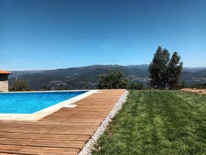 a swimming pool with a wooden deck next to a yard at Quinta das Mirandas Nature in Oliveira de Frades