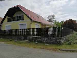 uma casa amarela com uma cerca preta e uma parede de pedra em Fitt Vendégház em Sümeg