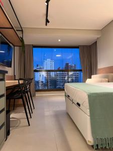 a bedroom with a bed and a desk and a large window at Barra Premium residencial in Salvador