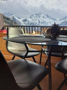 STUDIO 2 ALPES STYLE CHALET au PIED DE TELESIEGE DU DIABLE في لي دوز آلب: طاولة زجاجية وكراسي على شرفة مغطاة بالثلج وجبال