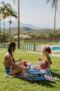 two girls sitting on a blanket on the grass at Suítes Romanetto com Piscina e Vista - Antonina in Antonina