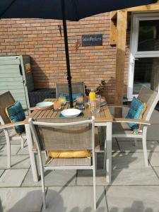 una mesa y sillas con una sombrilla en el patio en The Woodpeckers - Alresford Essex, en Alresford
