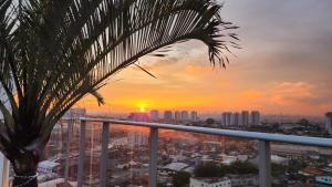 um pôr-do-sol a partir de uma varanda com uma palmeira em Stay GRU - Loft 2 Completo próx GRU airport - Guarulhos em Guarulhos