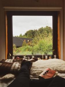 a person laying on a bed looking out a window at Tinyhouse Pichi I - vida lenta en Patagonia Costa in Calbuco