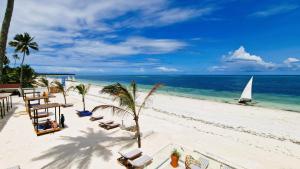 a beach with chairs and a sailboat in the ocean at Dream of Zanzibar Resort & Spa - Premium All Inclusive in Uroa