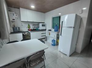 a white kitchen with a table and a refrigerator at Apartamento com três suítes em Garanhuns próximo ao Parque Euclides Dourado in Garanhuns