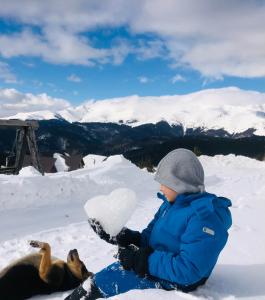 un niño pequeño sentado en la nieve con un perro en Pensiunea Casa Ancutei, en Ranca