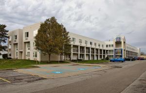 um grande edifício branco com um carro azul estacionado em frente em Motel 6-Buffalo, NY - Airport - Williamsville em Williamsville