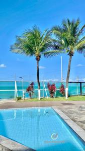 una piscina con dos palmeras y el océano en Ponta Negra Beach beira-mar ap 216, en Natal