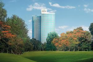 un edificio alto en el fondo con un campo y árboles en Hotel Mulia Senayan, Jakarta en Yakarta