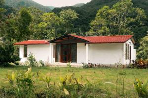 una pequeña casa blanca con techo rojo en un campo en Riverside Cabin in Cumandá, near Baños, Ecuador, en Mera