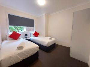 two beds with red pillows in a room at Eastwood Furnished Apartments in Sydney