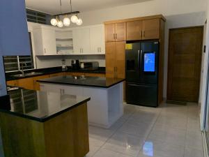 a kitchen with a black refrigerator and wooden cabinets at Villa de Lujo con Picsina Privada in San Pedro de Macorís