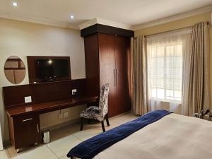 Dormitorio con cama, escritorio y TV en Booth Suite Hotel Mafikeng en Mafikeng