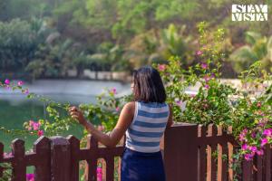 una donna appoggiata a una staccionata che guarda l'acqua di StayVista's Timber Cottage - Cozy Cottages with Indoor Games a Wādhiware