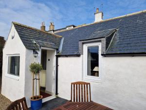 a white house with a window and two chairs at Coopers Cottage in Peterhead