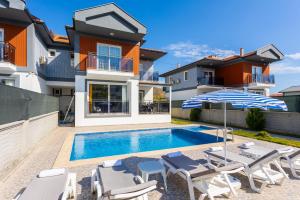 a swimming pool with chairs and an umbrella next to a house at Villa Sasha 2 in Ortaca