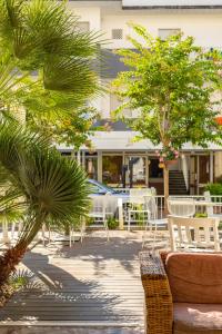 un patio con sedie bianche, tavoli e alberi di La Plata Hotel - con piscina a Riccione