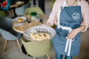 a woman in a blue apron holding a plate of food at Camping Passeier Glamping Aurum in Saltusio