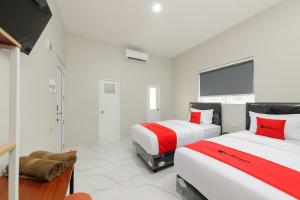 two beds in a room with white walls and red accents at RedDoorz near GSG UNILA Lampung in Hajimana