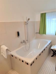 a white bath tub with a shower in a bathroom at A3 Hotel in Oberhonnefeld-Gierend