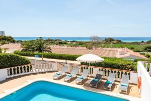 a pool with chairs and an umbrella and the ocean at Villa María in Son Bou