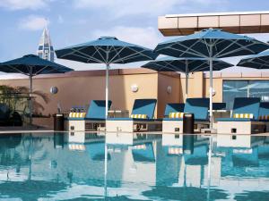 una piscina con sillas azules y sombrillas en un edificio en Pullman Dubai Jumeirah Lakes Towers, en Dubái