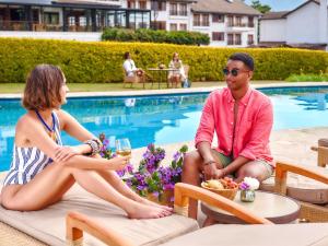 Ein Mann und eine Frau sitzen neben einem Pool in der Unterkunft Fairmont Mount Kenya Safari Club in Nanyuki