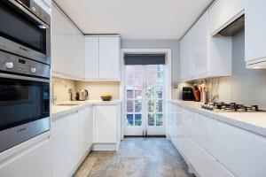 a kitchen with white cabinets and a large window at Veeve - Pine Glow Perfection in London