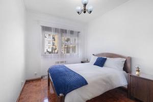 a white bedroom with a bed with a blue blanket at Cozy and Vintage Apartment in Carcavelos