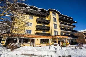 a yellow building with snow in front of it at Hotel Pinzgauerhof by Alpeffect Hotels in Zell am See
