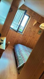 Ce lit se trouve dans une chambre en bois dotée d'une fenêtre. dans l'établissement FratoscanoHouse DOLOMITI Villaggio Veronza val di Fiemme max 4pax by fdnfashion, à Carano