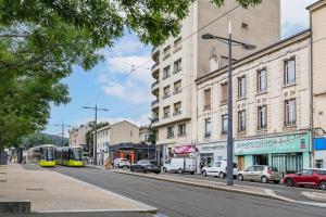 eine Stadtstraße mit Autos, Bussen und Gebäuden in der Unterkunft Harmonie 3 Chambres - spacieux in Saint-Étienne
