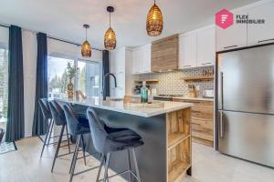 a kitchen with a counter with chairs and a refrigerator at Le Blanc Bouleau de Portneuf / Private Hot tub in Pont-Rouge