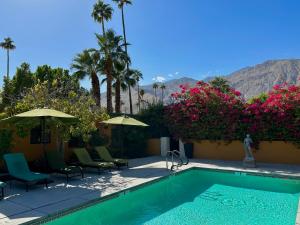 a swimming pool with chairs and umbrellas and flowers at Vista Grande Resort - A Gay Men's Resort in Palm Springs