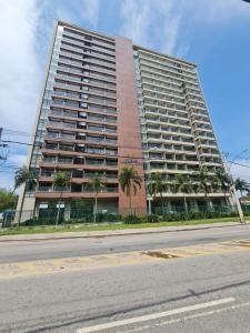 a tall building with palm trees in front of a street at Suíte com varanda em Via Premiere - Rio centro in Rio de Janeiro