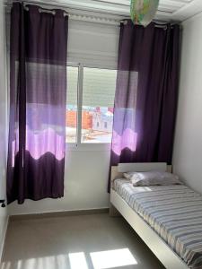 a bedroom with purple curtains and a window at Appartandalus in Larache