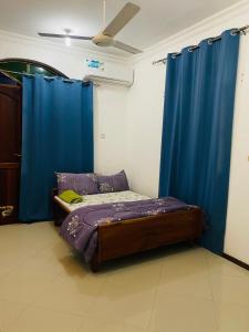 a small bedroom with a bed with blue curtains at Rafiki Guest House in Ngambo