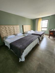 2 Betten befinden sich in einem Zimmer mit grünen Wänden. in der Unterkunft Studio charmoso em Ponta Negra in Natal
