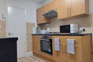 a kitchen with wooden cabinets and a stove and microwave at Comfortable 2 Mins from River & 5 Mins From Town in Kempston
