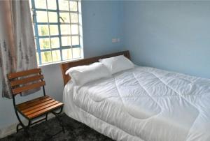 ein Schlafzimmer mit einem weißen Bett und einem Holzstuhl in der Unterkunft The D'Lux Home, Homa Bay in Homa Bay