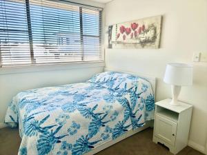 a bedroom with a blue and white bed and a lamp at Cosy unit with park & water view in Ballina