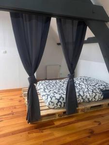 uma cama com cortinas azuis num quarto com pisos em madeira em Le chalet percheron em La Loupe