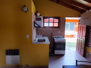 cocina con paredes amarillas, fregadero y fogones en CABAÑA LOS SAUCES en San Clemente del Tuyú