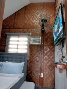 a bedroom with a bed and a tv and a wall at JHULLIE’S BREEZY HUT in Tagaytay