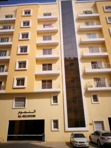 een hoog geel gebouw met een auto ervoor geparkeerd bij Al Nujoom Apartment, Al Qurum in Wuţayyah