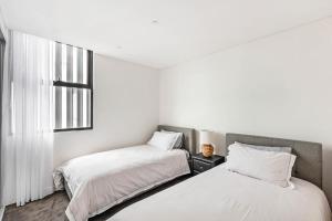two beds in a room with white walls and a window at Shellharbour Lakeview Apartment in Barrack Point