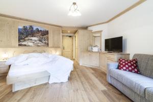 a bedroom with a bed and a couch and a tv at Dorfhotel Beludei in Santa Cristina in Val Gardena